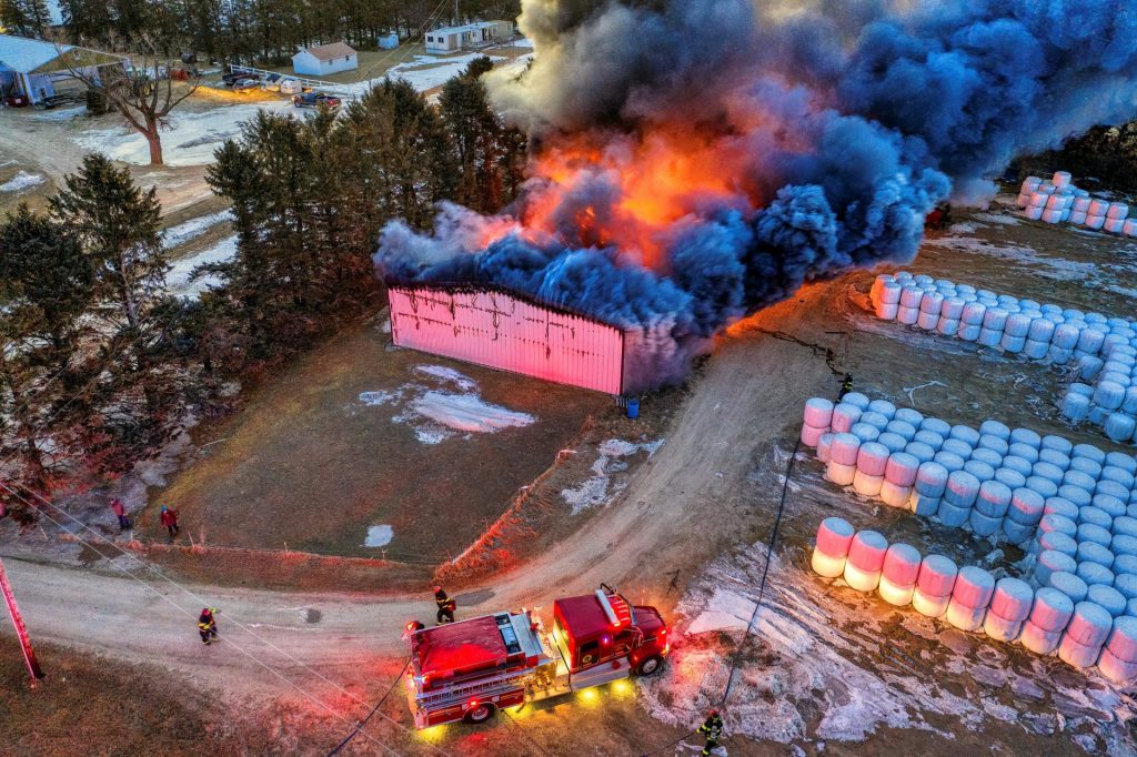 Firefighters respond to a burning barn in rural winter landscape.