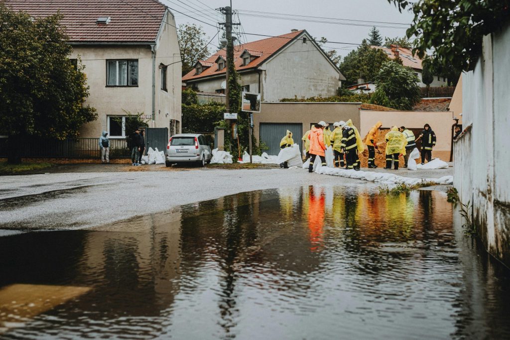 Emergency workers in rain gear manage floodwaters in a suburban street.