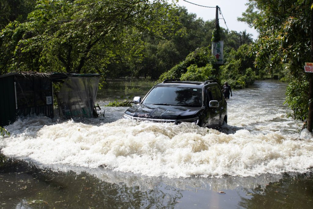 A black suv drives through a flooded street.